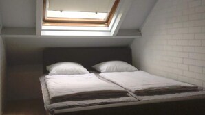 Une pièce dotée d’une lucarne, d’un lit avec une literie blanche et d’un mur en briques blanches.
