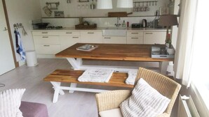 Une cuisine moderne avec des meubles blancs, une table à manger en bois et une chaise en osier.