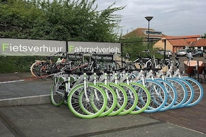 Uma área de estacionamento para bicicletas com várias bicicletas e uma placa que diz 'Fietsverhuur' e 'Fahrradverein'.