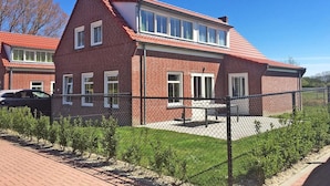 A brick house with a sloped roof, a fenced yard, and a paved driveway.