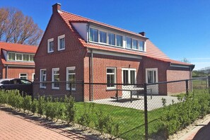 A brick house with a sloped roof, a fenced yard, and a paved driveway.