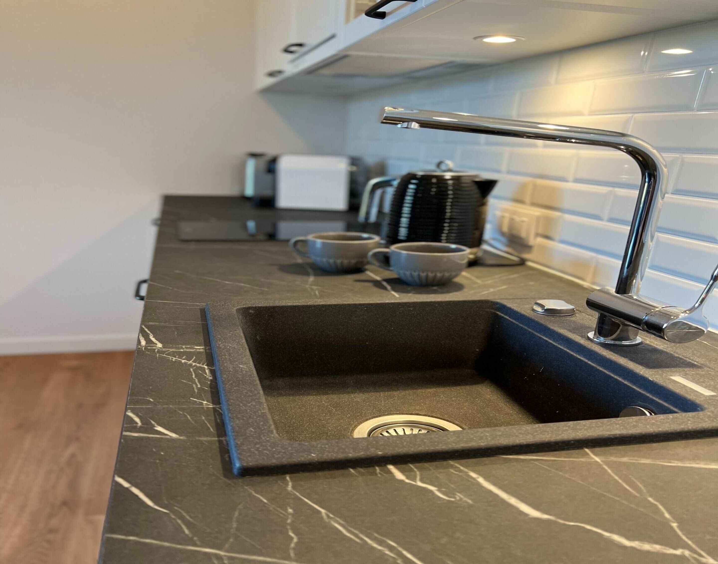 A kitchen with a black marble countertop, a sink, and a stainless steel faucet.