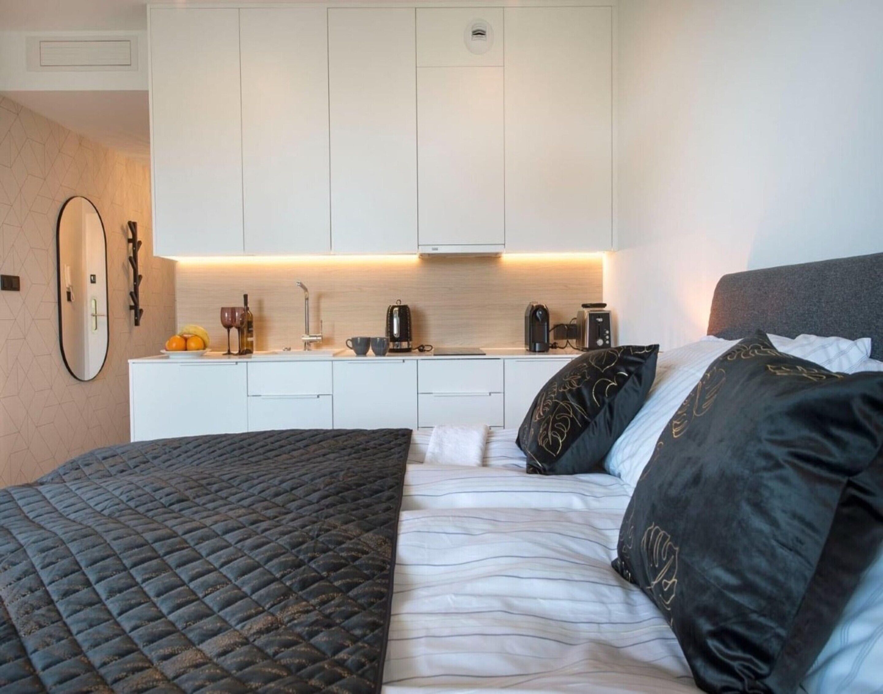 Une chambre à coucher comprenant un lit, des oreillers, une table de chevet et un coin cuisine équipé d’un évier, d’une cuisinière et d’une machine à café.