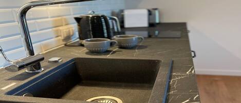 A kitchen with a black marble countertop, a stainless steel sink, and a modern faucet.