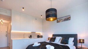 A modern hotel room with a large bed, a small kitchenette, and a dining area.