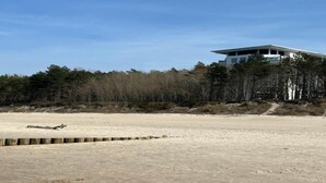 A sandy beach with a wooden barrier and a modern building with a flat roof in the background.