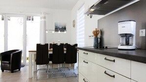 A modern kitchen with white cabinets, a coffee maker, and a dining area with black chairs. - Ferienhaus, Boiensdorf (Boiensdorf)