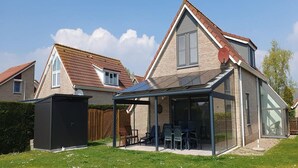 A modern house with a glass-enclosed patio, a black shed, and a well-maintained lawn. - Eco-Friendly Holiday Home (Breskens)