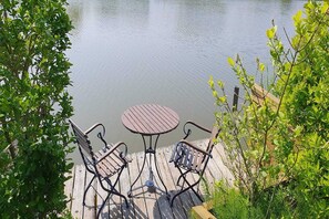 A wooden deck with a round table and two chairs, overlooking a calm body of water.