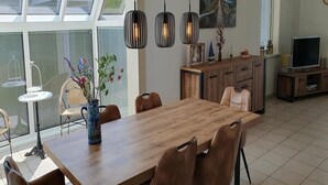 A modern dining area with a wooden table, chairs, pendant lights, a vase with flowers, and a TV on a wooden cabinet. - Eco-Friendly Holiday Home (Breskens)