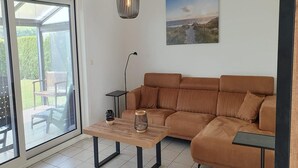 A living room with a brown sofa, a wooden coffee table, a floor lamp, and a view through a glass door to an outdoor area. - Eco-Friendly Holiday Home (Breskens)