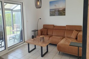 A living room with a brown sofa, a wooden coffee table, a floor lamp, and a view through a glass door to an outdoor area. - Eco-Friendly Holiday Home (Breskens)