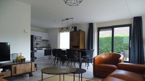 A modern living room with a sofa, a TV, and a dining area with chairs and a table.