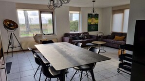 A modern living room with a dining table, sofas, and a large window.
