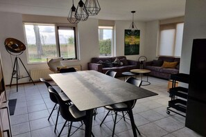 A modern living room with a dining table, sofas, and a large window.