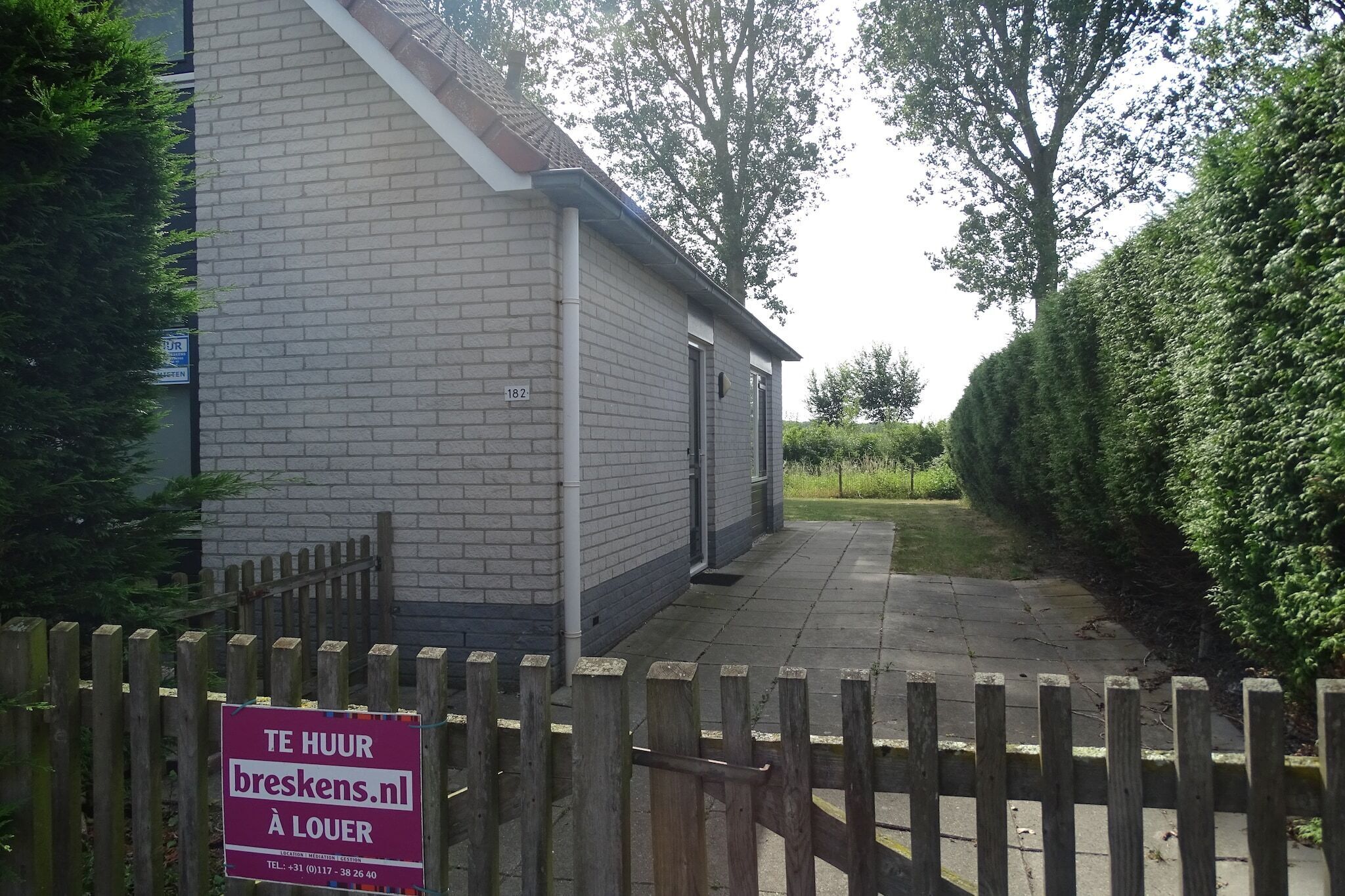 A building with a brick facade, a wooden fence, and a sign indicating a location in 'breskens.nl'.