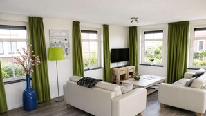 A modern living room with two white sofas, a coffee table, a TV, and a desk.