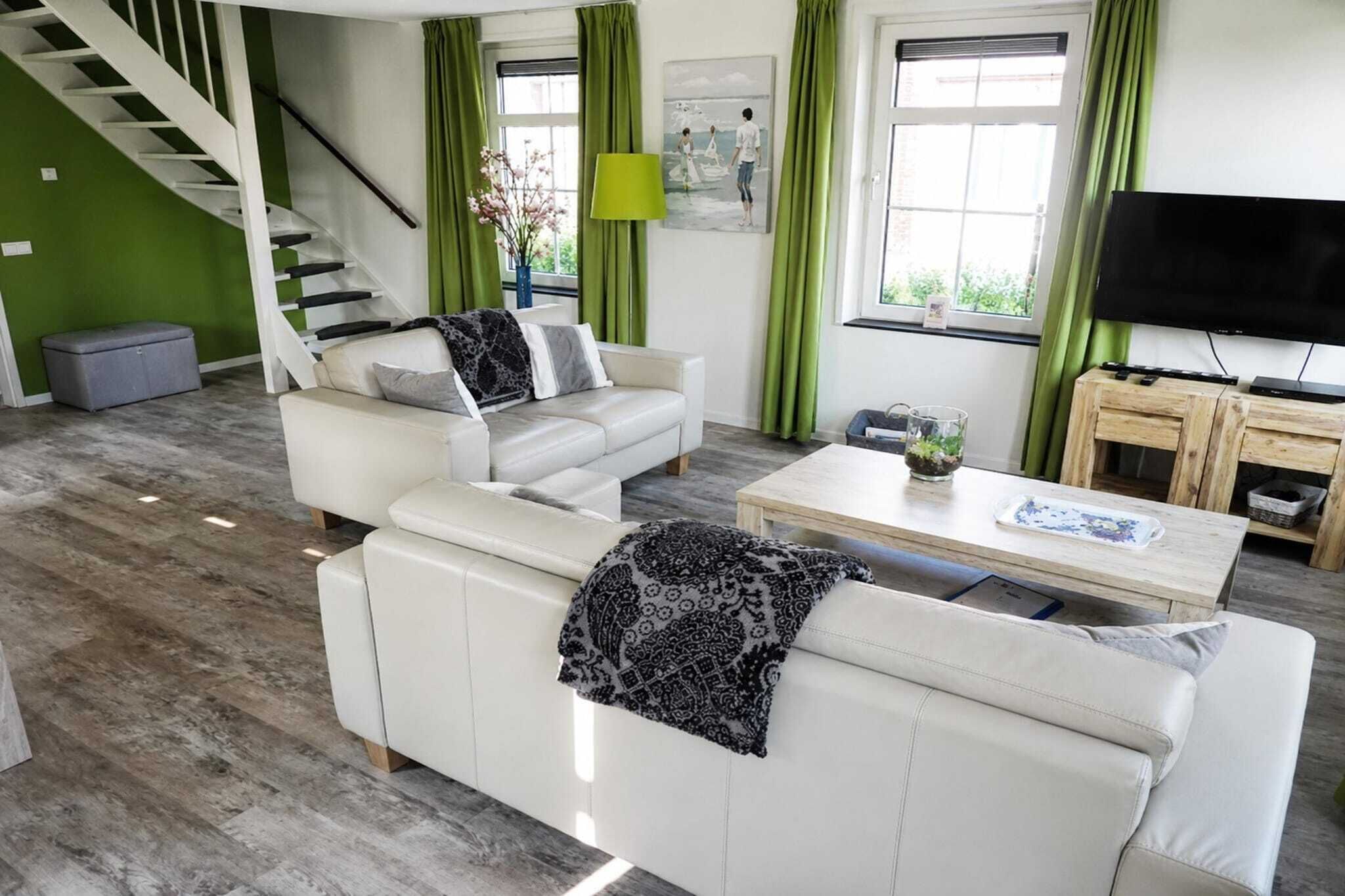 Ein modernes Wohnzimmer mit Treppe, grünen Vorhängen, einem Flachbildfernseher und einem Couchtisch.