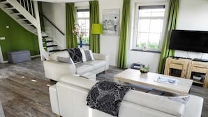 A modern living room with a staircase, green curtains, a flat-screen TV, and a coffee table.