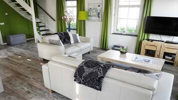 Ein modernes Wohnzimmer mit Treppe, grünen Vorhängen, einem Flachbildfernseher und einem Couchtisch.