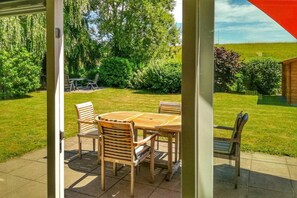 A patio with a table and chairs, surrounded by a grassy lawn and trees. - Bungalow in Breskens near Waterfront Beach (Breskens)