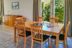 Un coin repas avec une table et des chaises en bois, un petit meuble et une fenêtre donnant sur un paysage verdoyant.