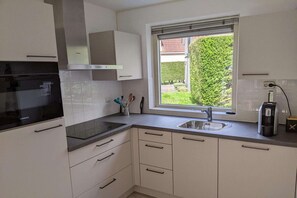 Une cuisine moderne avec des meubles blancs, une cuisinière noire, une fenêtre donnant sur un espace verdoyant et une machine à café.