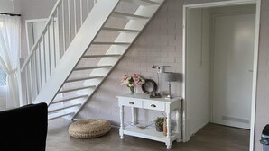 A staircase with white railings, a white console table with drawers, a wicker ottoman, and a door with a vent.