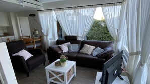 A living room with a sofa, armchair, TV, and a small table with a plant.