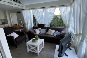 A living room with a sofa, armchair, TV, and a small table with a plant.
