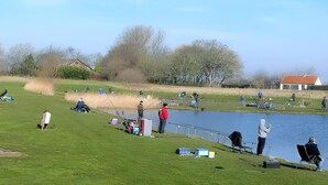 A lakeside fishing area with people fishing, a small building, and a grassy field. - Spacious Stay Near the Sea (Breskens)