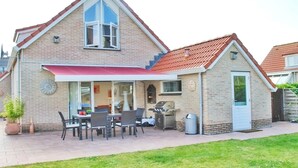 Ein zweistöckiges Haus mit Terrasse, Grill und kleiner Gartenhütte.