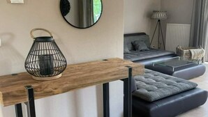 A modern living room with a wooden console table, a black metal lantern, a grey sofa with cushions, a round mirror, and a floor lamp. - Spacious Stay Near the Sea (Breskens)