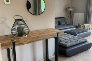 A modern living room with a wooden console table, a black metal lantern, a grey sofa with cushions, a round mirror, and a floor lamp. - Spacious Stay Near the Sea (Breskens)