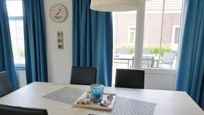 A dining area with a table, chairs, a clock, and curtains. - Holiday Home in Breskens near the Beach (Breskens)