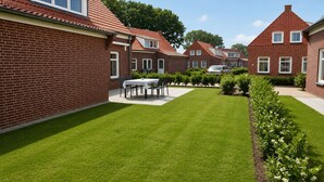 A residential area with brick houses, a well-maintained lawn, and a dining table set outdoors. - Holiday Home in Breskens near the Beach (Breskens)