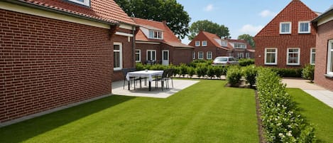 A residential area with brick houses, a well-maintained lawn, and a dining table set outdoors.