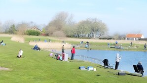 A lakeside fishing area with people fishing, boats, and a small house in the background. - Holiday Home in Breskens near the Beach (Breskens)