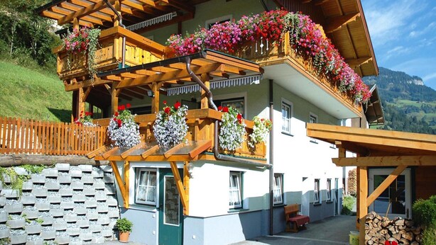 A chalet with wooden balconies, flower boxes, and a stone wall. - Chalet in Grossarltal With Panoramic Views (Grossarl)