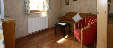 A cozy living room with a wooden floor, a red armchair, a checkered sofa, a small table, and a radiator.