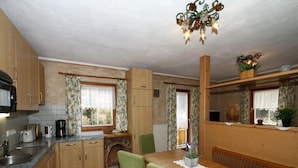 A compact kitchen with wooden cabinets, a dining table with green upholstered chairs, and a chandelier. - Chalet in Grossarltal With Panoramic Views (Grossarl)
