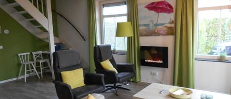 A living room with a staircase, two black chairs with yellow cushions, a beige sofa, a white coffee table, and a TV on a stand.
