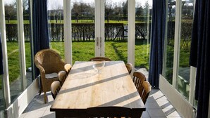 A conservatory with a wooden table and chairs, large glass doors, and a view of a grassy area.