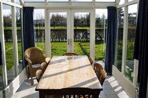 A conservatory with a wooden table and chairs, large glass doors, and a view of a grassy area.