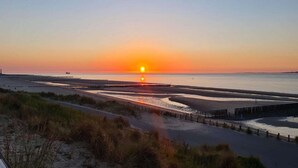 A sunset over a beach with a boardwalk and dunes.
