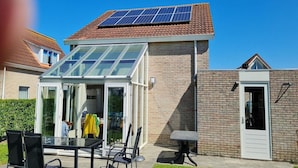 A house with a solar panel roof, a glass-enclosed patio, and a brick exterior.