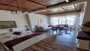 Une pièce spacieuse avec un plafond en bois, un lit recouvert d’une couverture rouge, un canapé, une table à manger avec des chaises et une grande fenêtre avec des rideaux.