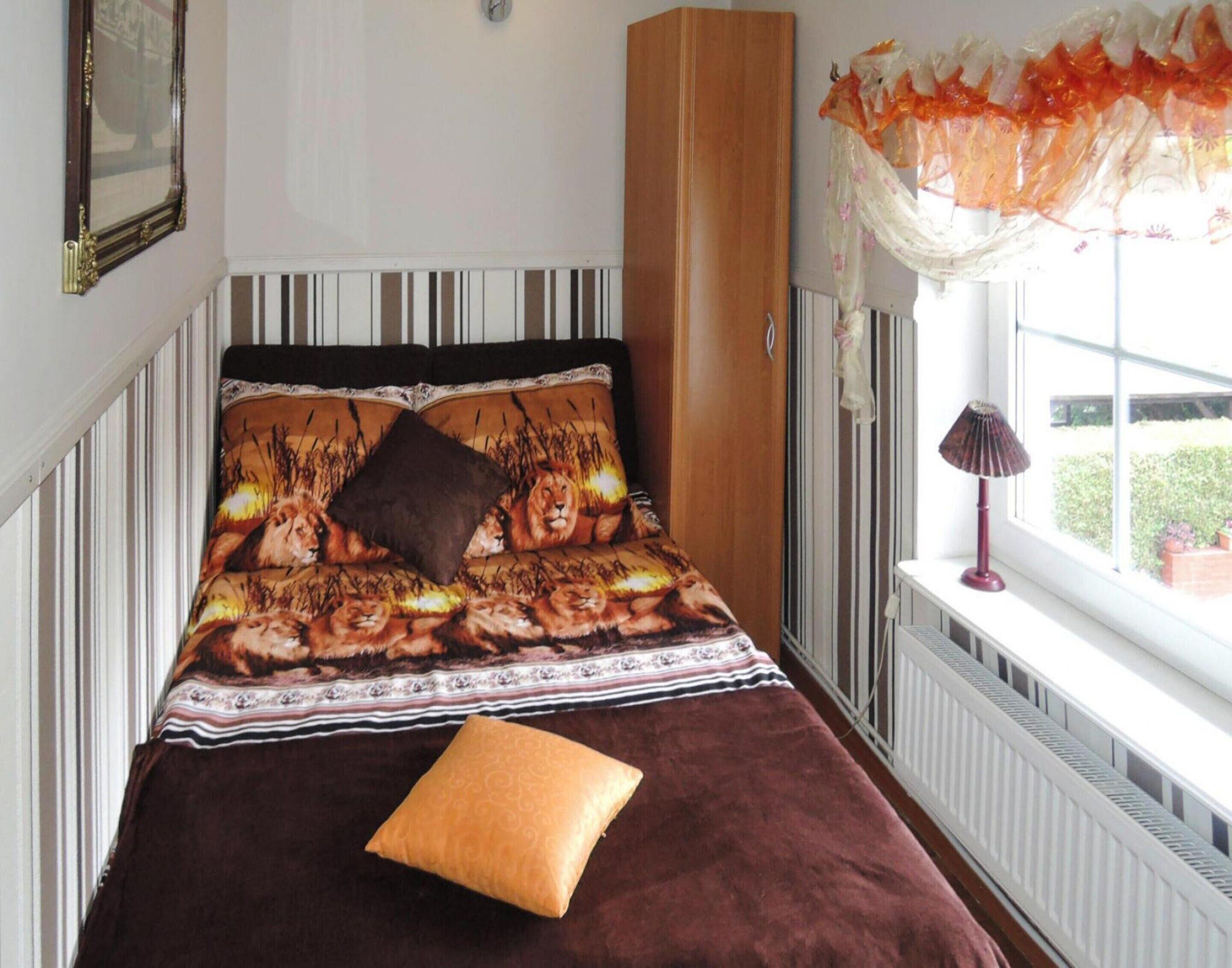 Een bed met een bedspread met luipaardprint, een bruin kussen en een raam met uitzicht op groen.