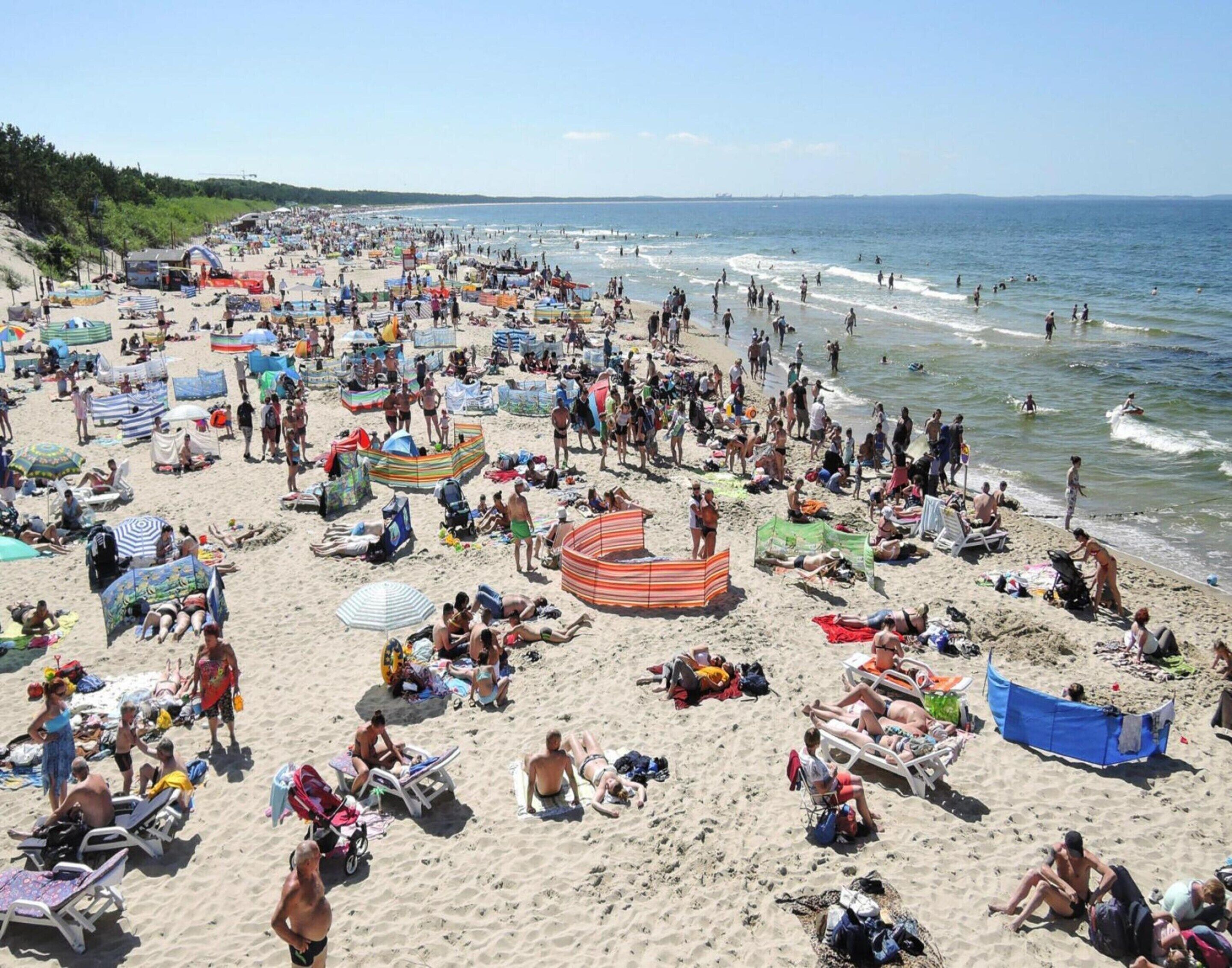 Ein voller Strand mit vielen Liegestühlen und Sonnenschirmen.