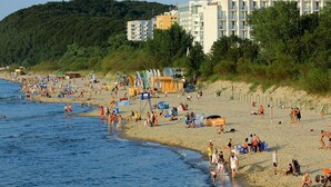 Une plage avec des gens, des tentes et un bâtiment en arrière-plan.